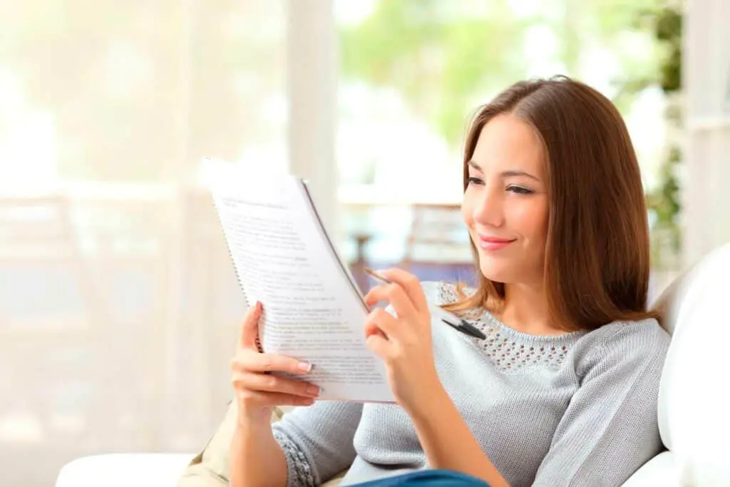 Girl making notes with a pen while reading a book.