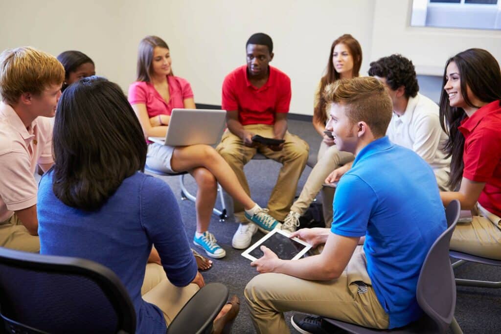 Young people sitting in a circle on chairs and chatting