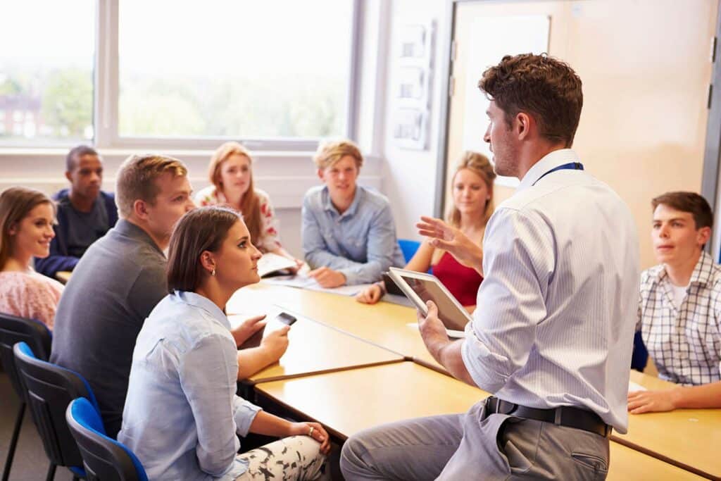 A young man standing and speaking to a group of young people who are seated and listening to him