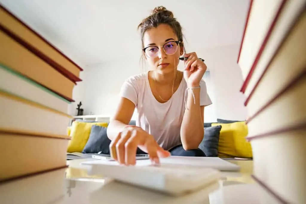 A student reading and taking notes at home with a pile of books