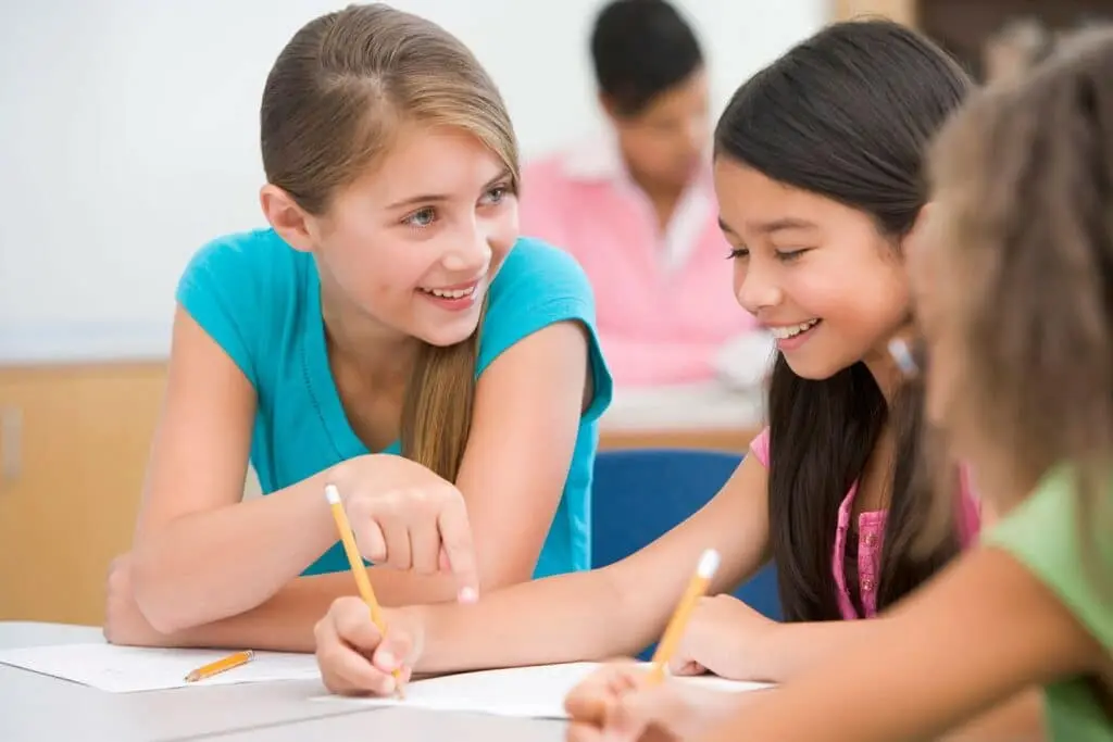 schoolgirls in class writing with pencils and socializing.