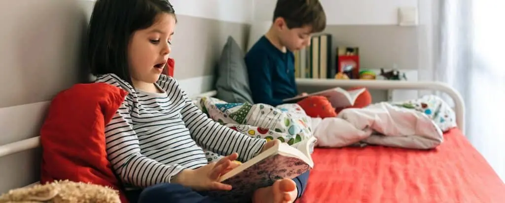 Two children reading books on a bed