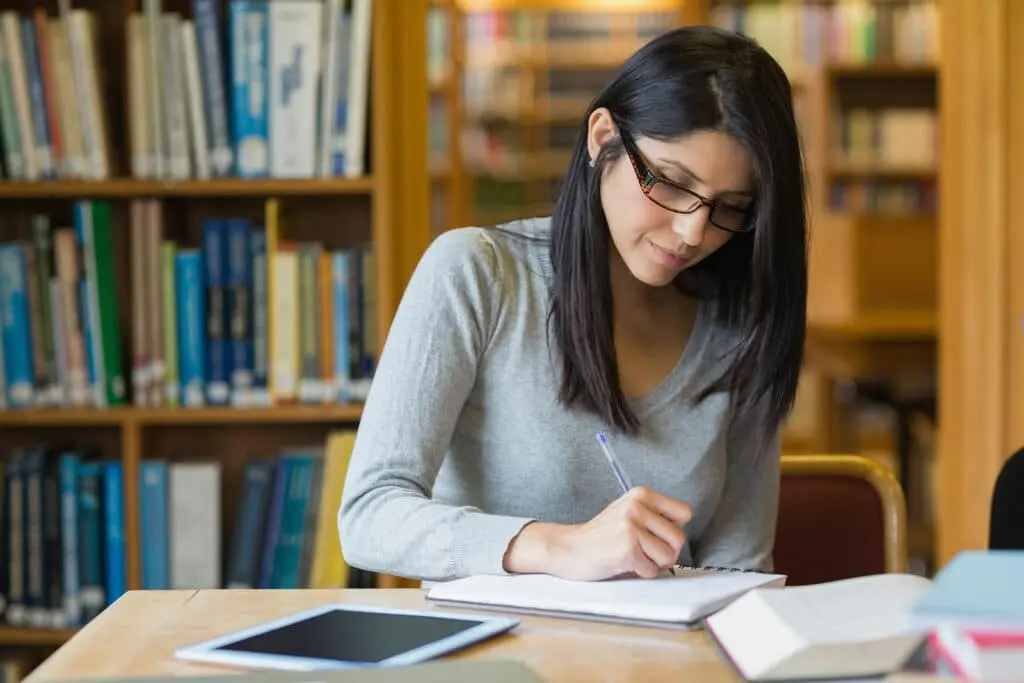 A woman writes in a notebook in the library.