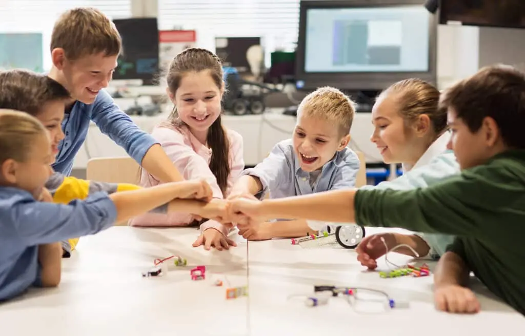 Smiling children at a classroom table bumping fists together