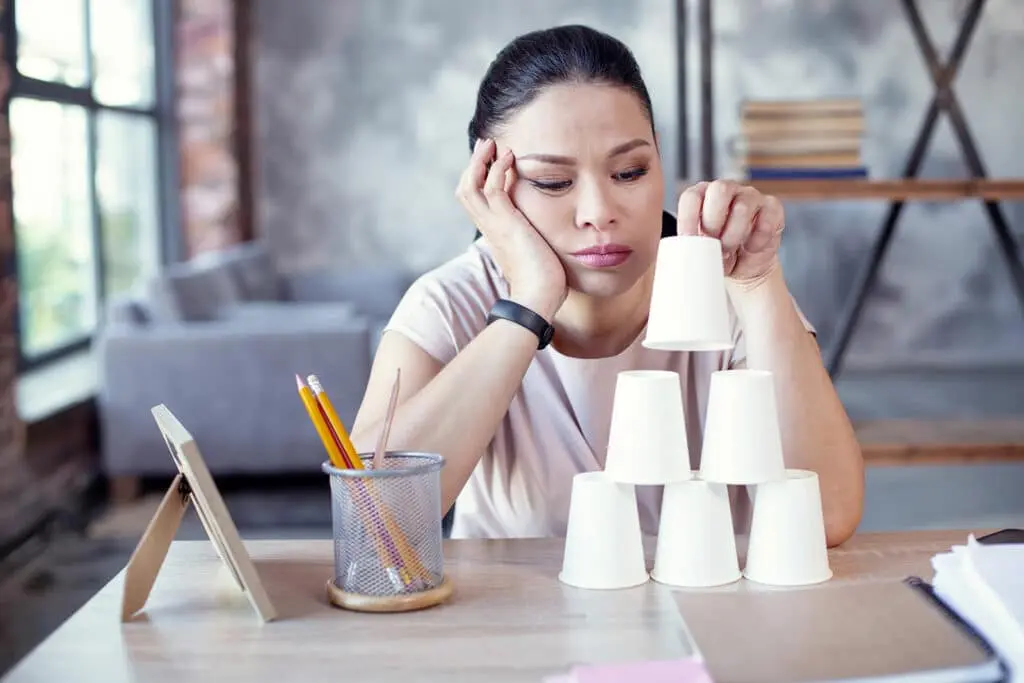 the girl with the pensive face is building a pyramid out of paper cups.