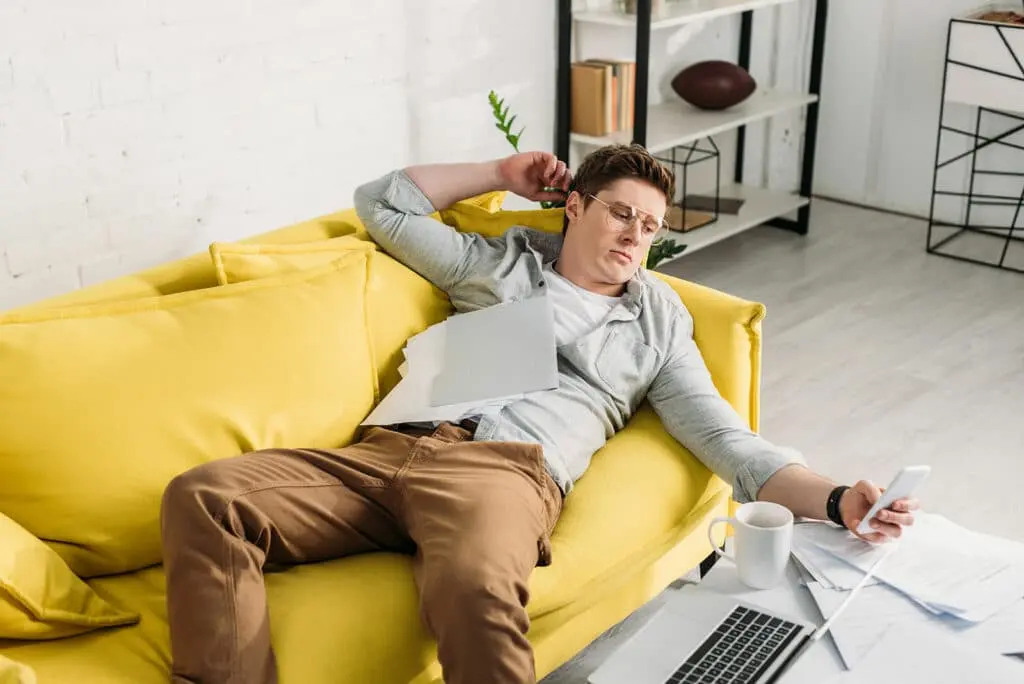 a man lying on a yellow couch looking at his phone.